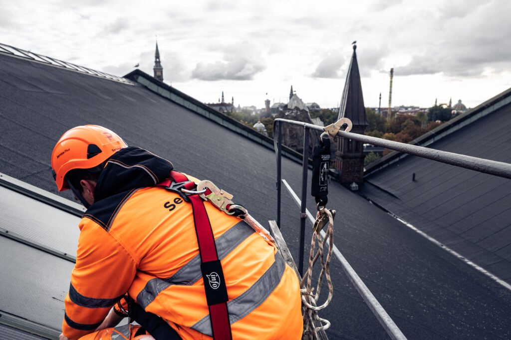 Tagdækker i sikkerhedssele arbejder på tag i højden – professionel montering af nyt tag.