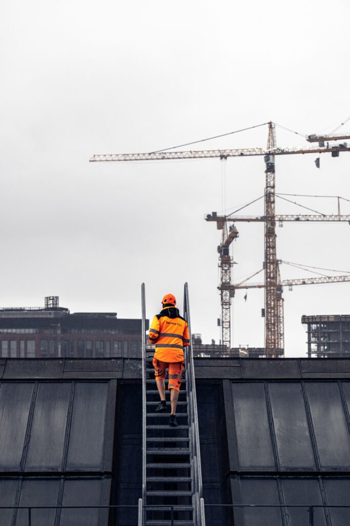 Mand i arbejdstøj på vej op ad stige til tag – klar til tagrenovering i højden.