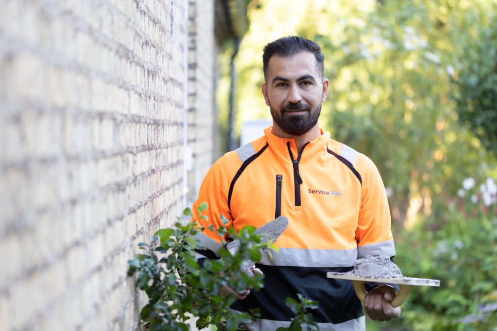 Håndværker arbejder ved murstenshus i forbindelse med renovering – en del af opgaven med nyt tag til kunden.
