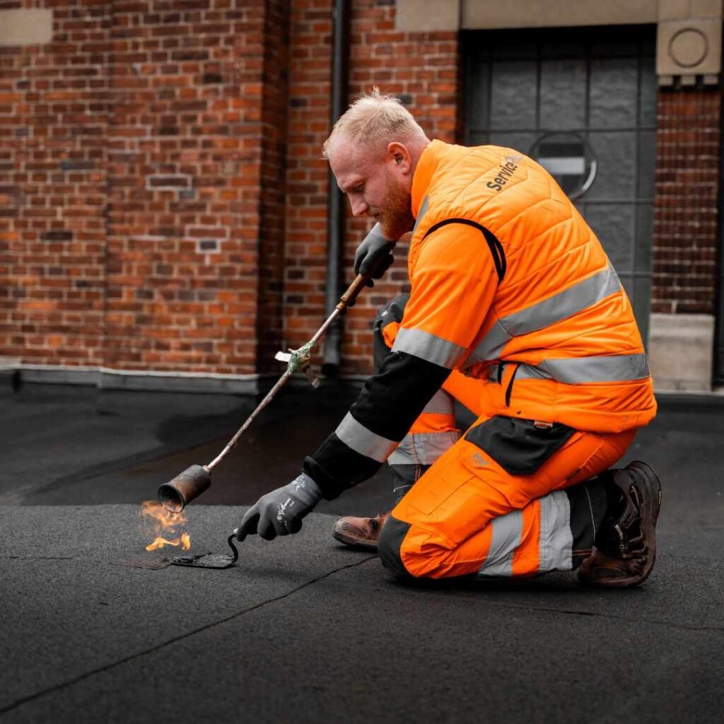 Tagdækker i arbejdstøj arbejder med tagpap på bygning – kontakt os i dag og få et godt tilbud på nyt tag.